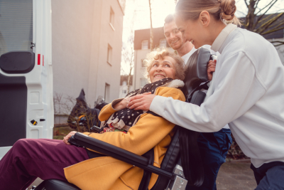 woman touching the hand of an elderly woman while helping her to get in the van while in wheelchair