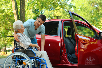 man assisting elderly woman in wheelchair get in the red car